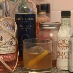 A glass of Old Fashioned cocktail garnished with an orange peel, made with whiskey, bitters, simple syrup, and a cherry.