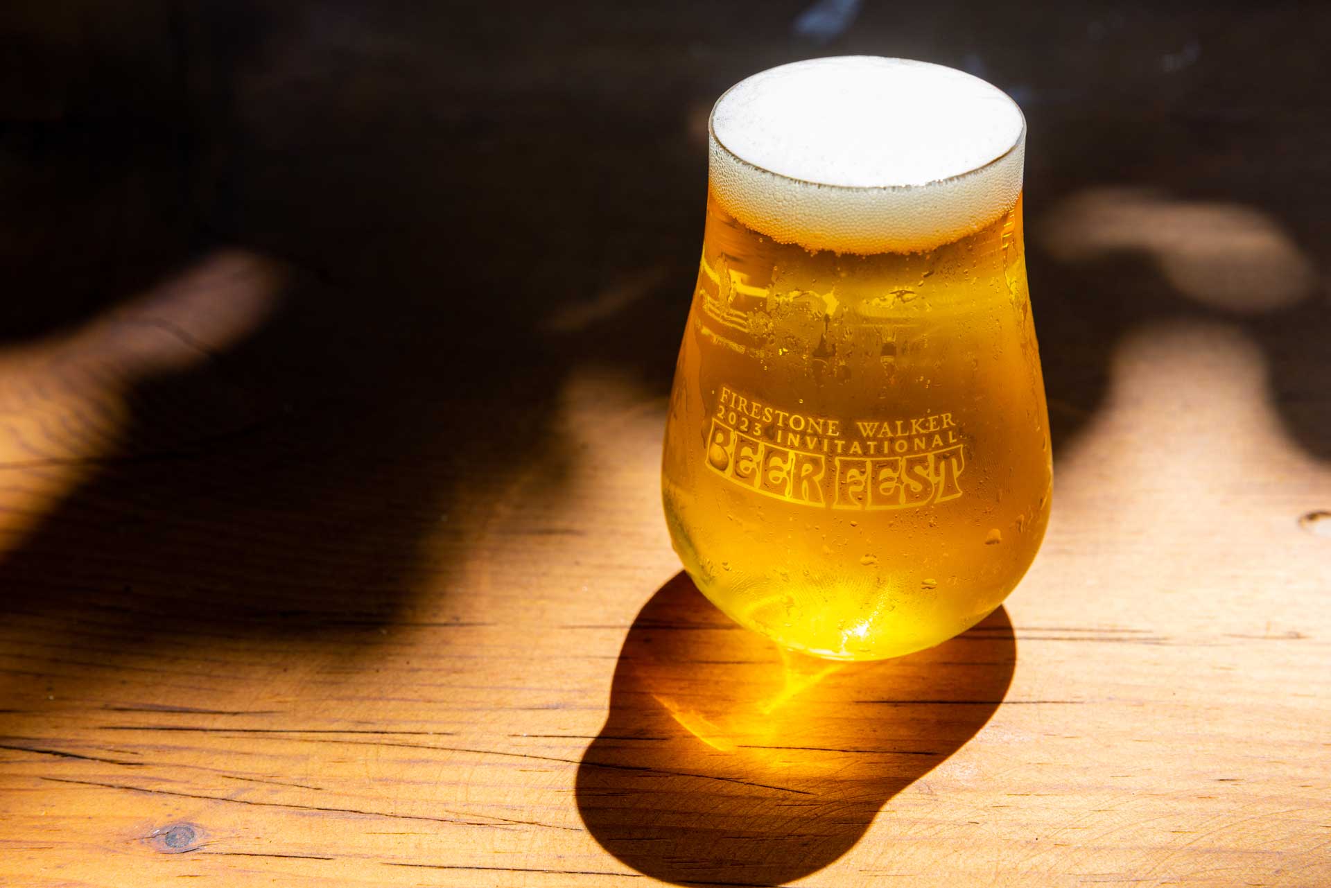 ice cold beer with reflection coming from the sun that produces a bright yellow orange color coming from a glass with engraving of Firestone Walker 2023 Invitational Beer Fest