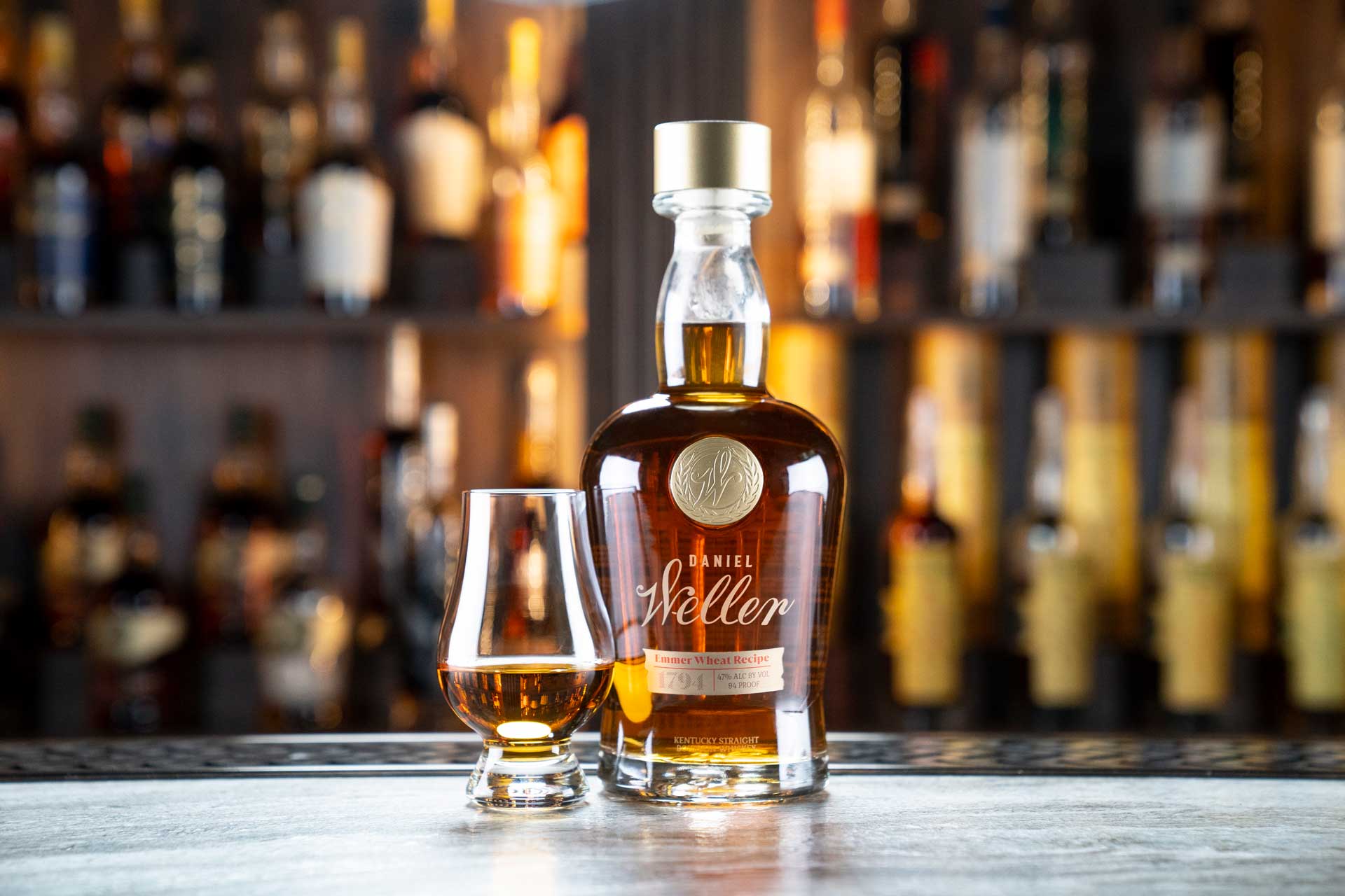 Daniel Weller Emmer Wheat recipe bourbon whiskey bottle beside a drinking glass.