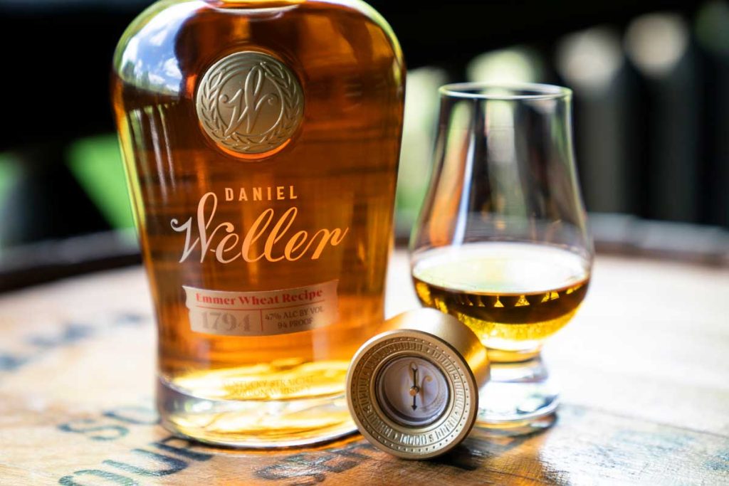 Daniel Weller Emmer Wheat recipe bourbon whiskey bottle beside a drinking glass and a compass