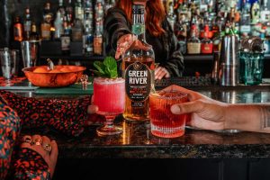 A pink cocktail in a coupe glass and garnished with a sprig of mint and a red cocktail in a rocks glass.