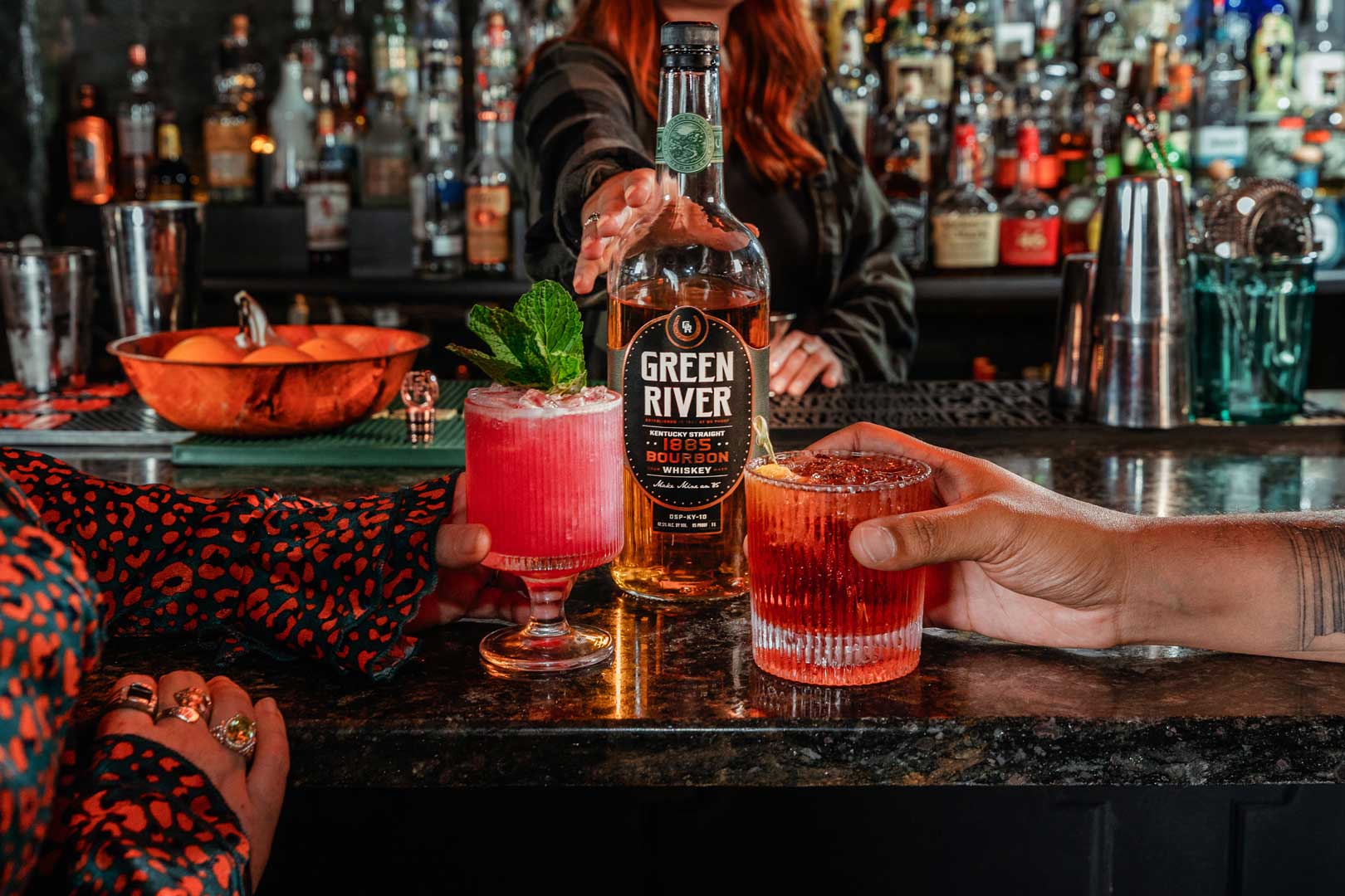 A pink cocktail in a coupe glass and garnished with a sprig of mint and a red cocktail in a rocks glass.