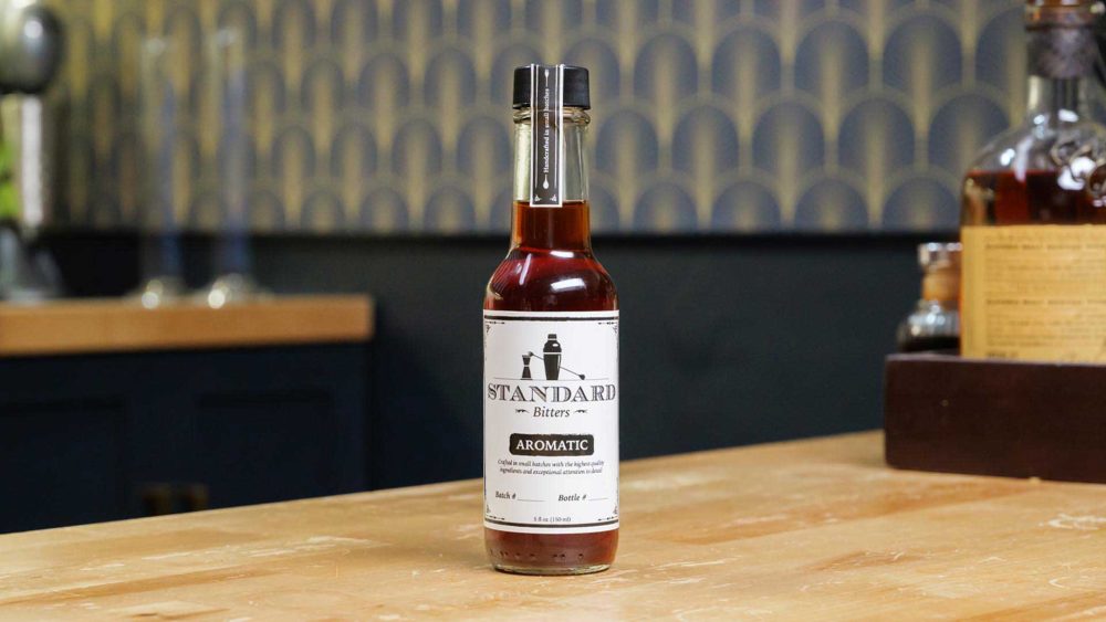 A bottle of Standard Bitters Aromatic bitters on a wooden counter.