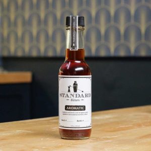 A bottle of Standard Bitters Aromatic bitters on a wooden counter.
