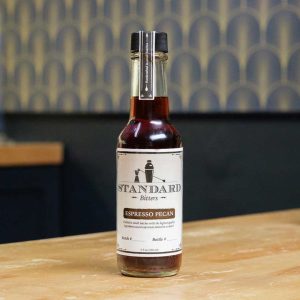 A bottle of Standard Bitters Espresso Pecan bitters on a wooden counter.