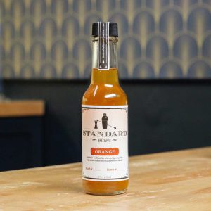 A bottle of Standard Bitters Orange bitters on a wooden counter.