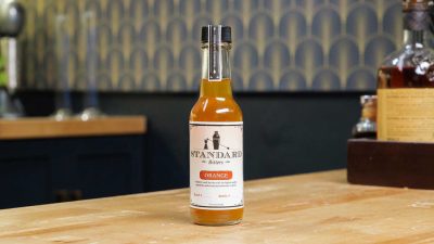A bottle of Standard Bitters Orange bitters on a wooden counter.