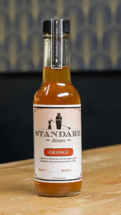A bottle of Standard Bitters Orange bitters on a wooden counter.