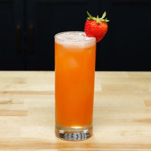 A tall glass filled with a red cocktail, ice cubes and garnished with a strawberry.